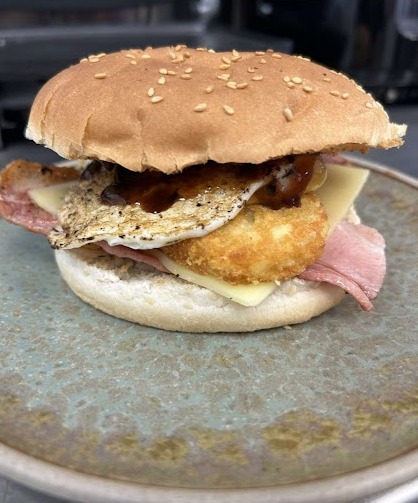 A burger with egg, hash brown, bacon and cheese on a sesame bun